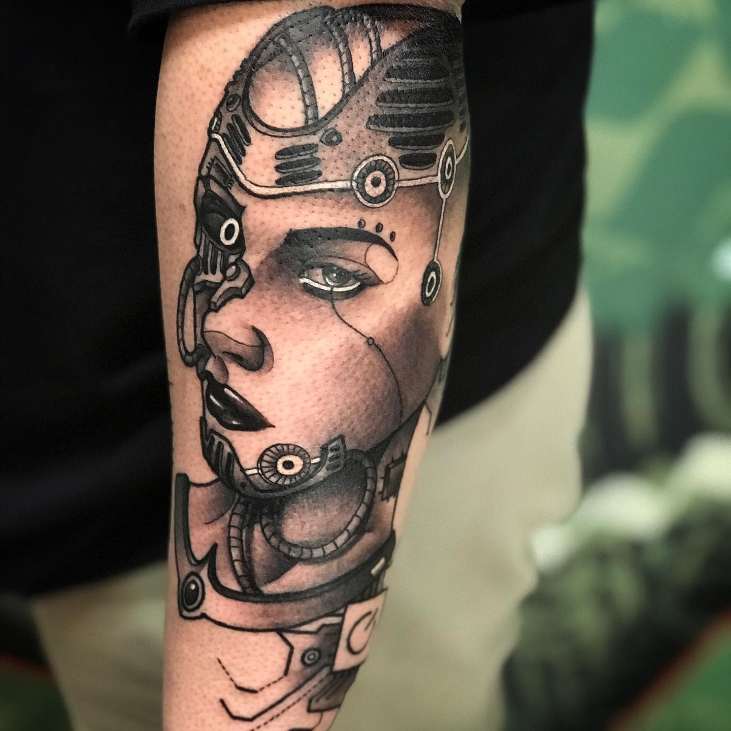 Detailed cyberpunk tattoo on forearm featuring a futuristic female face with mechanical elements